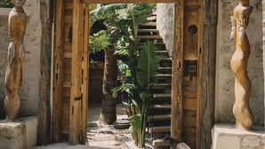 A rustic entrance with a sign reading "SUARE," flanked by wooden sculptures and a cobblestone path leading inside. - Suare Alaçatı (Cesme)