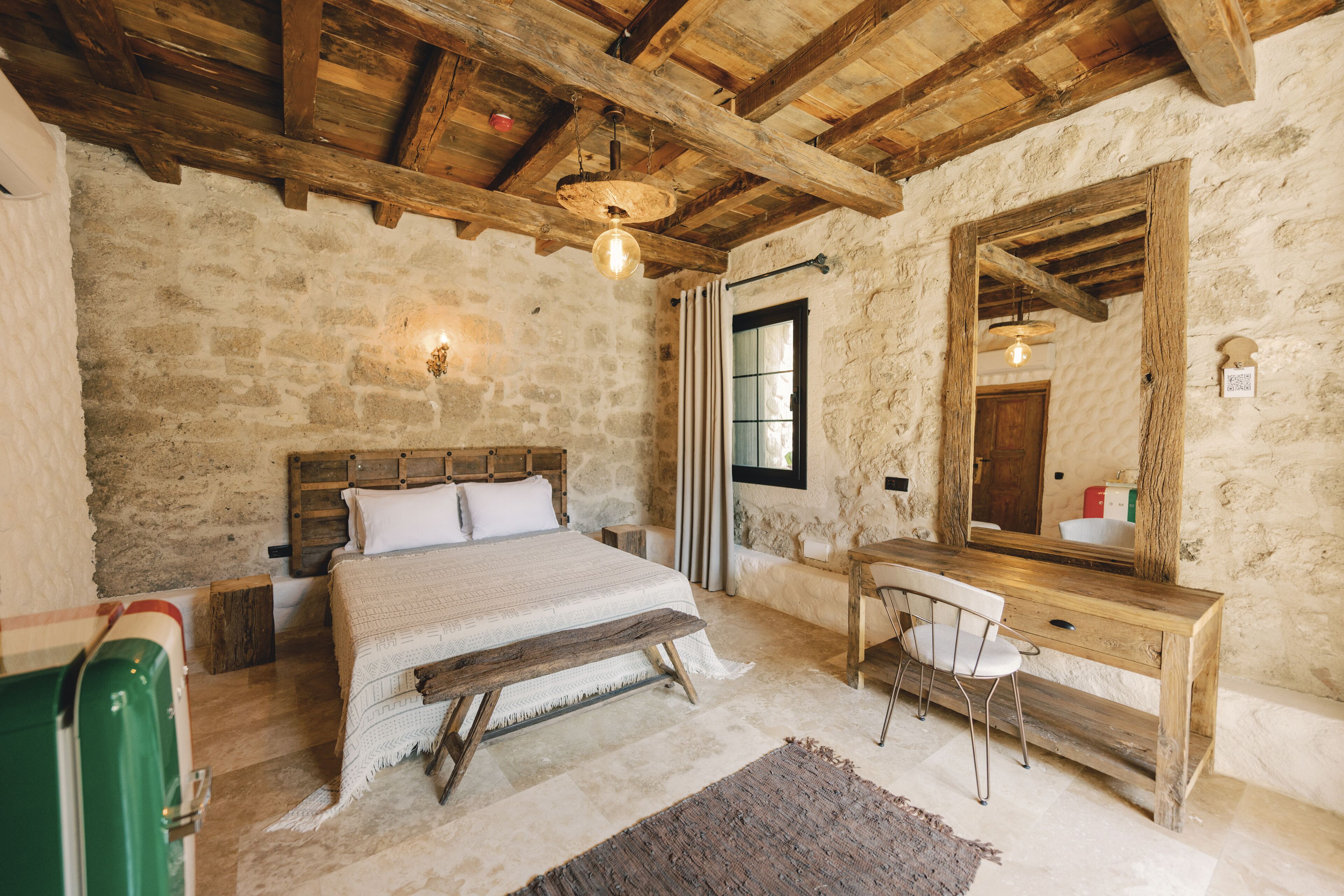 A rustic bedroom with a wooden bed, a wooden desk, and a large mirror.
