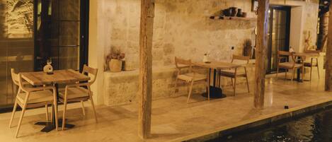 A rustic outdoor dining area with wooden tables and chairs, a stone wall, and a number '2' sign.