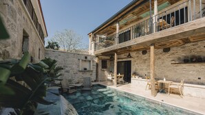 A pool area with a wooden deck, outdoor furniture, and a stone wall. - Suare Alaçatı (Cesme)