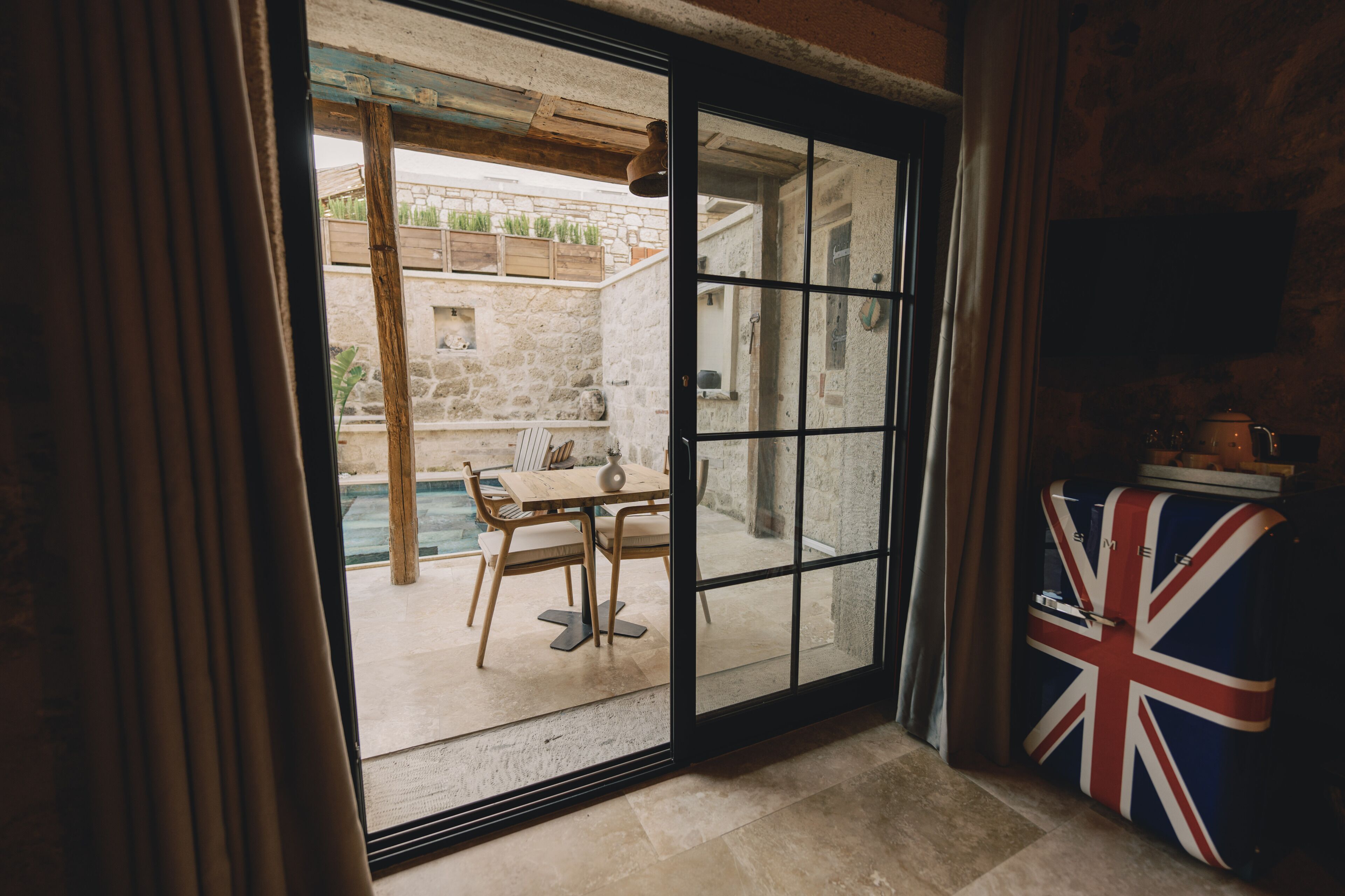 A room with a large sliding glass door leading to an outdoor area with a pool and a wooden table.
