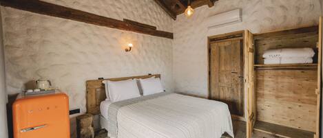 A rustic bedroom with a wooden bed, a vintage orange refrigerator, and a wooden wardrobe.