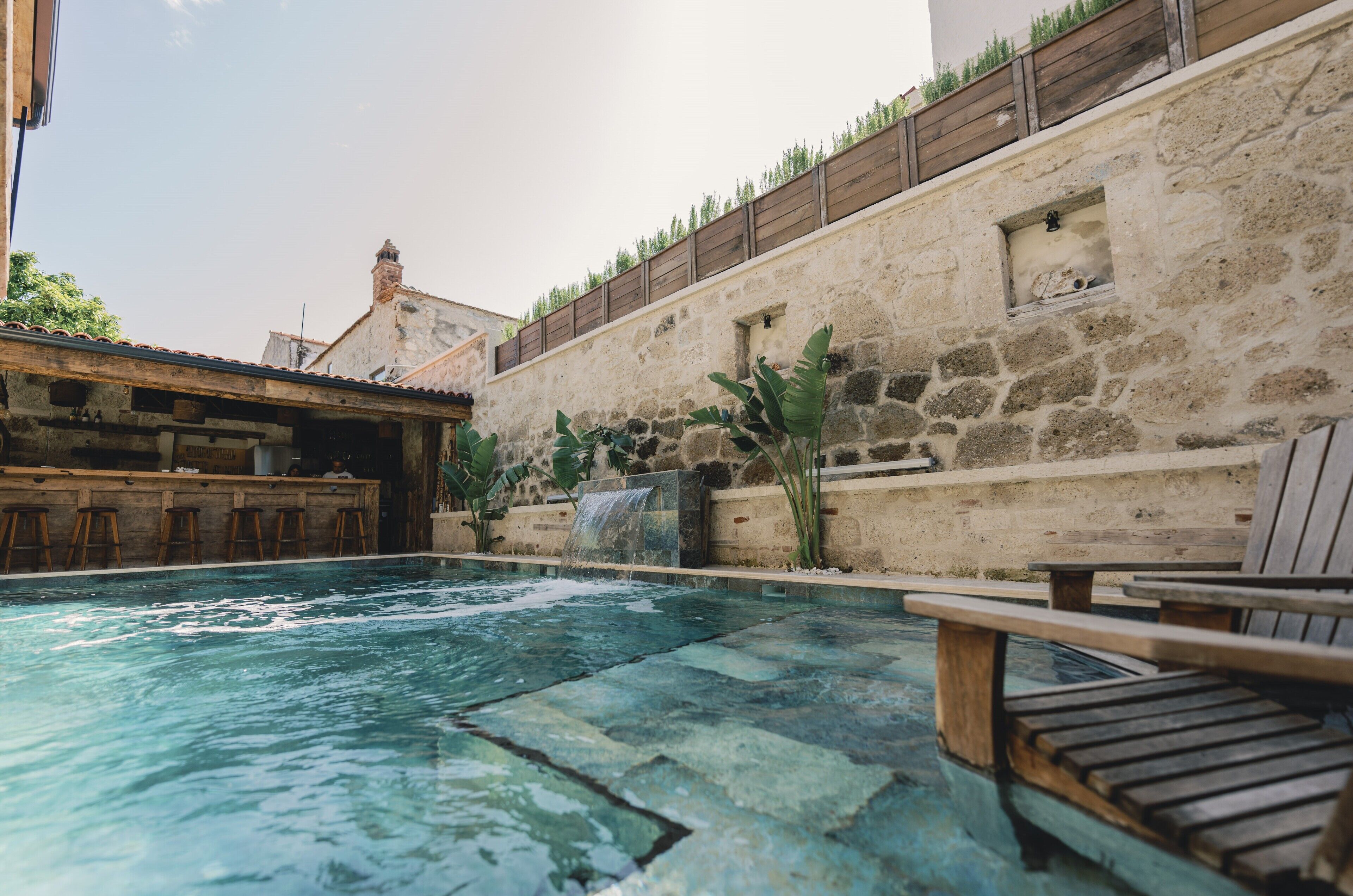 A pool area with a stone wall, wooden deck, and a waterfall feature.