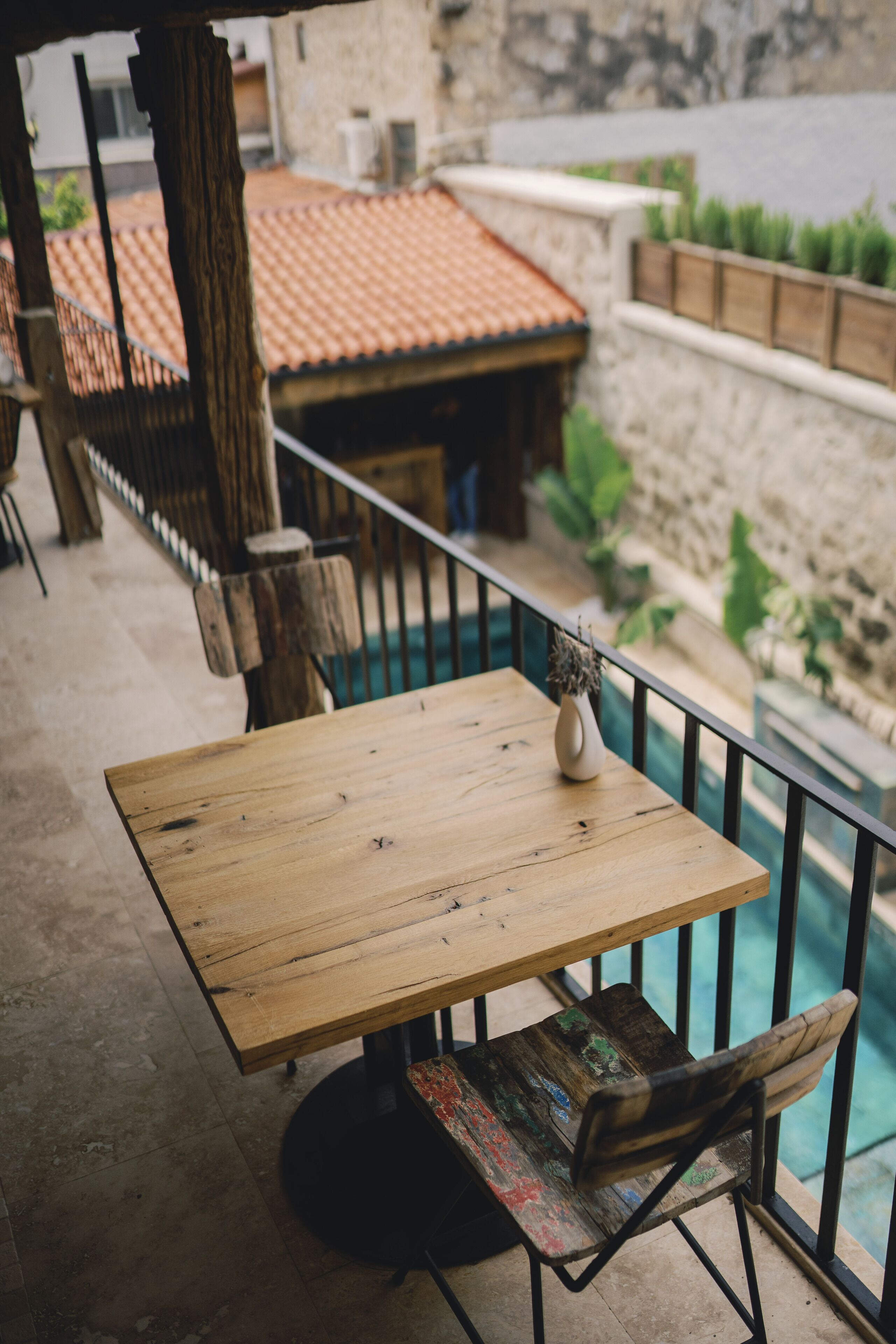 Ein Holztisch mit einer Vase, einem Stuhl und einem Geländer mit Blick auf einen Pool und Gebäude.