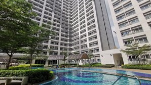 A high-rise residential building with a swimming pool and surrounding greenery. - 1BR Studio w/ Pool, Balcony, Near Airport&Hotspots (Taguig)