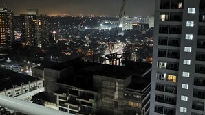 A nighttime cityscape with high-rise buildings, a construction crane, and a balcony railing. - 1BR Studio w/ Pool, Balcony, Near Airport&Hotspots (Taguig)