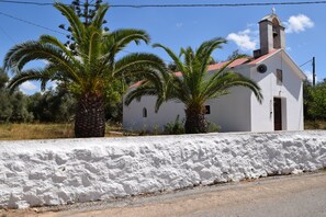 A white church with a bell tower, surrounded by palm trees and a white wall. - LOTUS villa in PRINES, private pool, near beaches, restaurants, Rethymno. (Prines, Rethymno)
