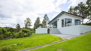 A modern house with a white exterior, large windows, and a grassy yard. - Swimming pool along the terrace, panoramic view surrounded by nature  (หางดง)