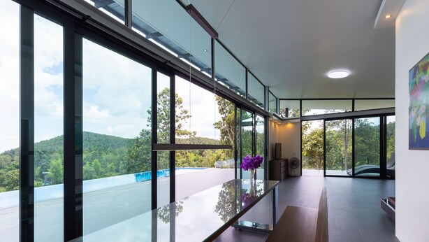 A modern interior with large glass windows, a wooden floor, and a vase with purple flowers. - Swimming pool along the terrace, panoramic view surrounded by nature  (หางดง)