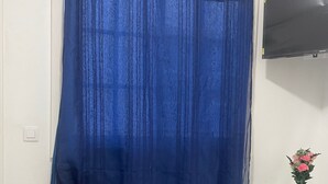 Una habitación con una cortina azul, un aparador de madera, una mesa de vidrio con un florero y un reloj en la pared.