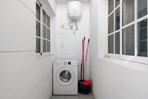 Une petite buanderie équipée d’un lave-linge, d’un chauffe-eau et d’un seau.