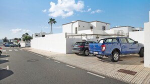 Vista de la calle con una camioneta azul estacionada junto a un edificio blanco, un paso de peatones y una palmera al fondo.
