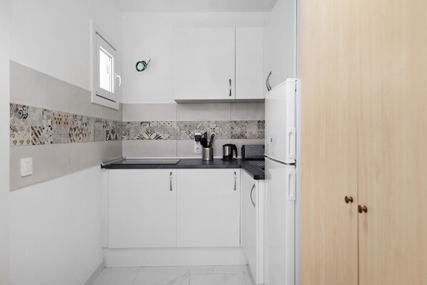 A compact kitchen with white cabinets, a black countertop, and a microwave.