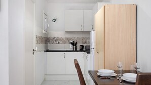 Cocina compacta con armarios blancos, una puerta de madera y una mesa de comedor dispuesta con platos y vasos.