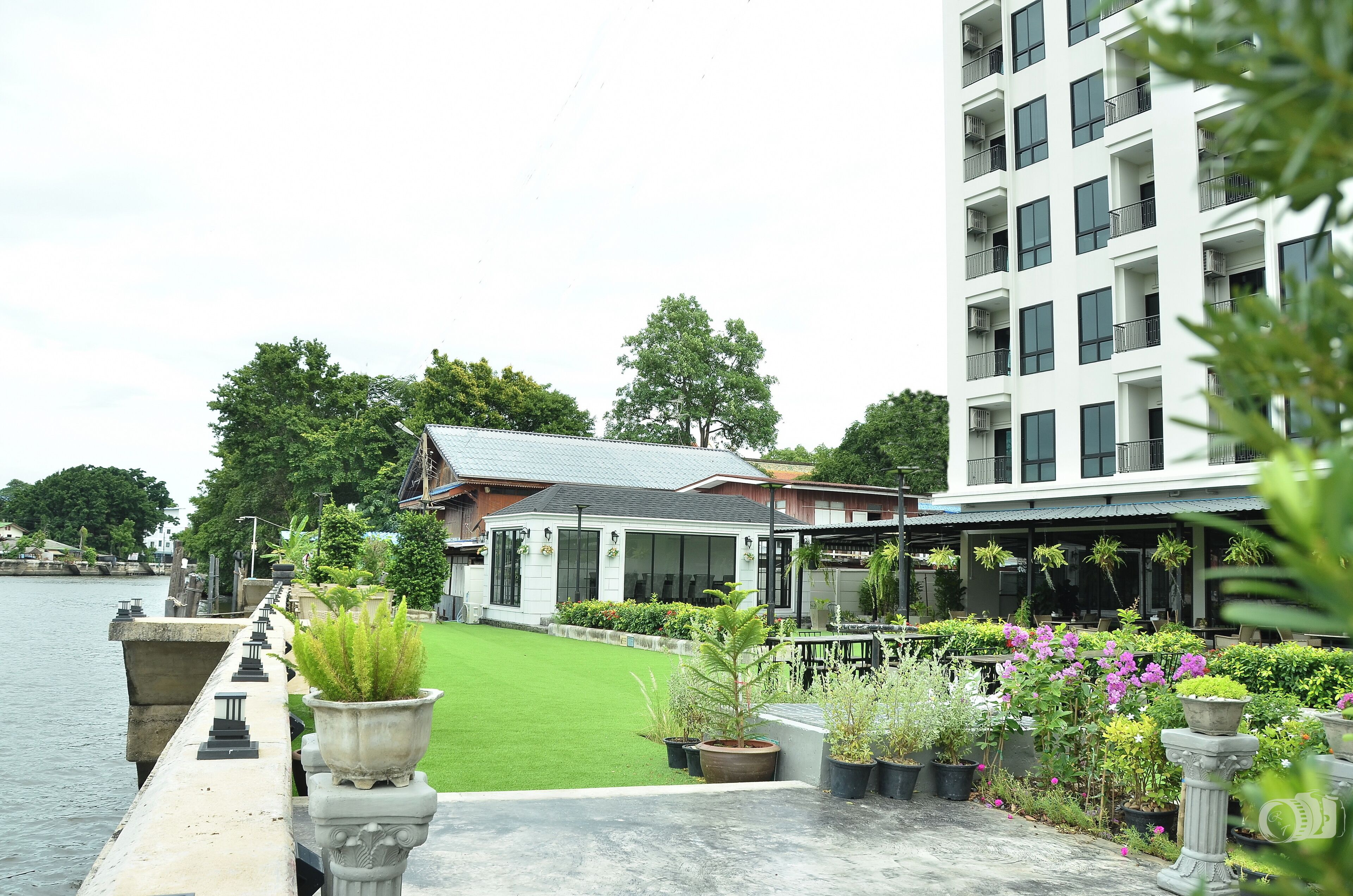 A waterfront hotel with a garden, a pool, and a modern building in the background.