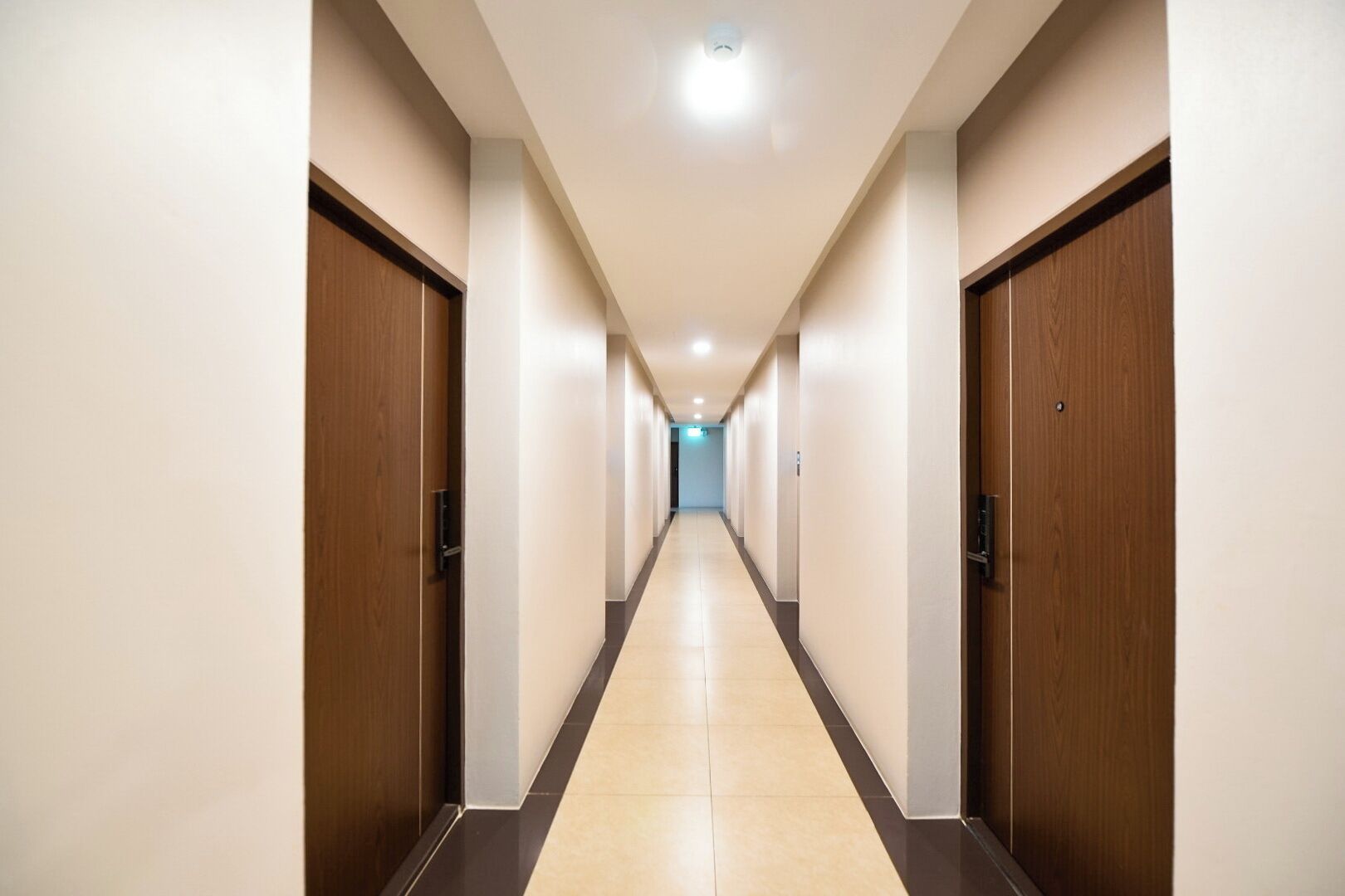 A long, narrow hotel corridor with wooden doors on both sides and a tiled floor.