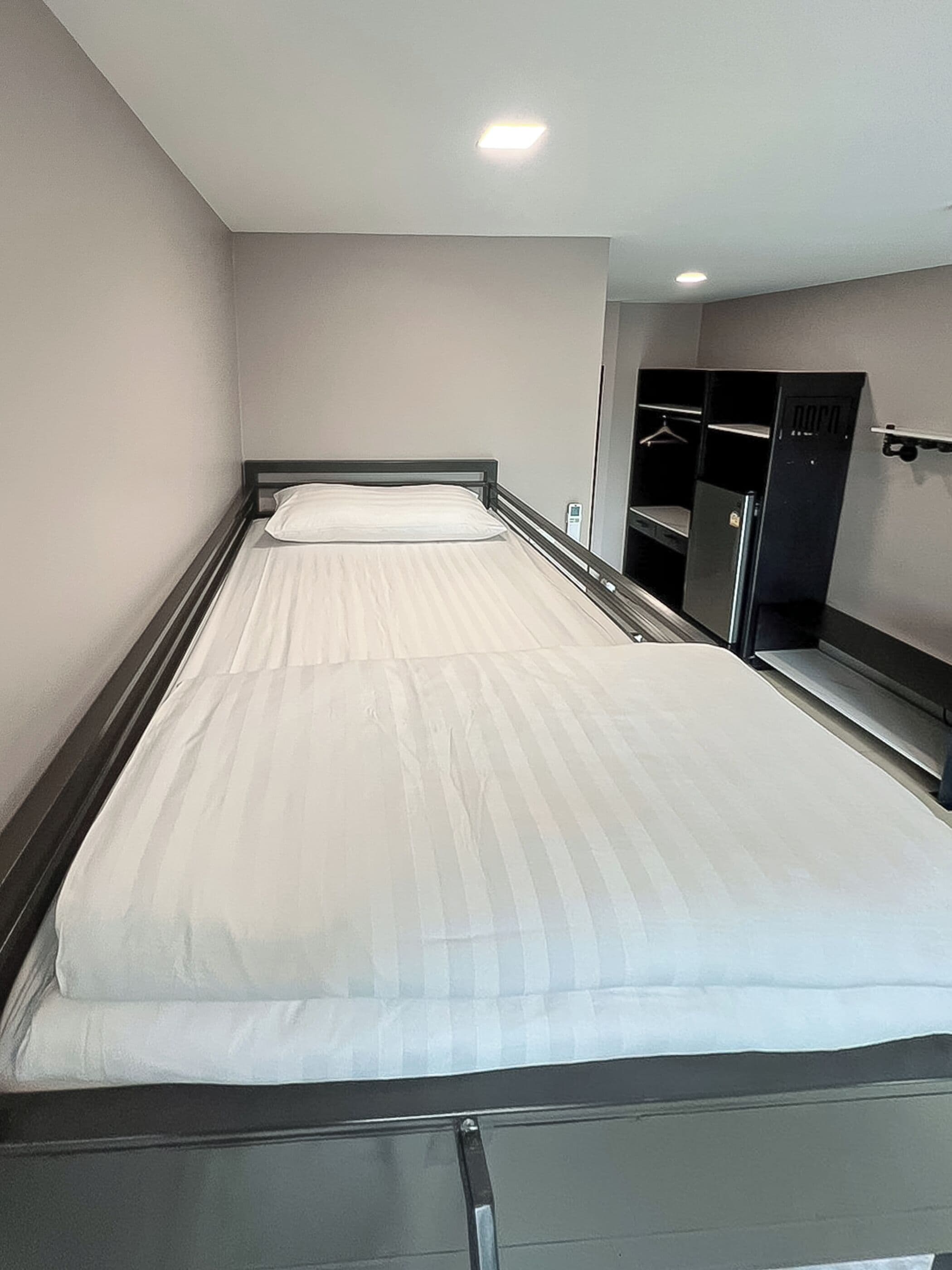 Een eenpersoonsbed met houten frame en een witte matras in een hotelkamer.