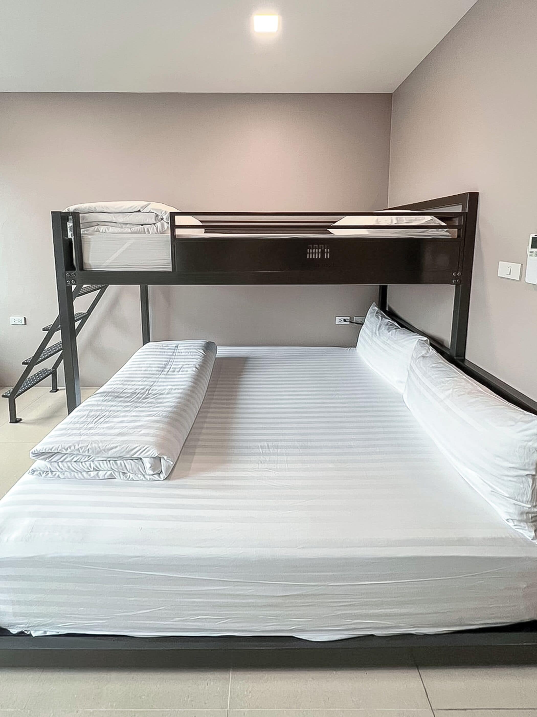 Un lit superposé avec un bureau et une chaise, une petite fenêtre et une prise de courant.