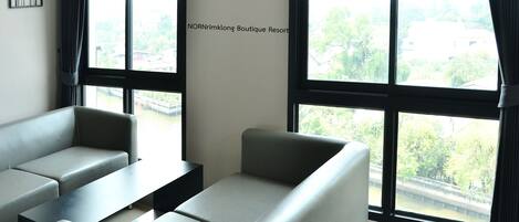 A modern room with grey sofas and a black table, large windows with curtains, and a wall sign reading "NORNrimklong Boutique Resort".