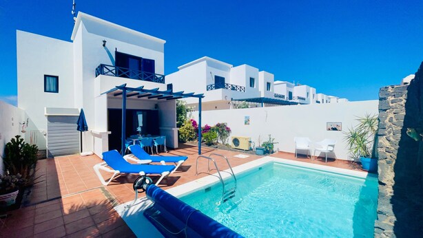 Ein moderner Poolbereich mit blauen Liegestühlen, einem Pool mit klarem Wasser und weißen Gebäuden im Hintergrund.