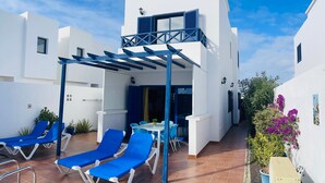 Eine moderne Terrassenanlage im Freien mit blauen Loungemöbeln, einem Tisch und einer Pergola.