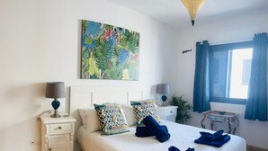 Ein ordentlich eingerichtetes Schlafzimmer mit einem Bett, zwei Nachttischen, einem Wandbild, einem Fenster mit Vorhängen und einem kleinen Tisch mit einer Schale.