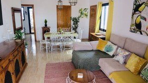 Ein Wohnzimmer mit einer Couch, einem Esstisch mit Stühlen, einem Couchtisch und einem Holzschrank.