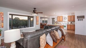 A modern living room with a leather sofa, a dining area, and a kitchen with wooden cabinets and a clock. - Private home on 40 acres surrounded by wide open space. (Vernon)