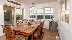 A dining room with a wooden table, six chairs, a chandelier, and large windows offering a view of the outdoors. - Private home on 40 acres surrounded by wide open space. (Vernon)