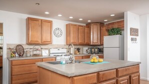 A kitchen with wooden cabinets, a stainless steel sink, a refrigerator, and a clock on the wall. - Private home on 40 acres surrounded by wide open space. (Vernon)