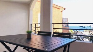Un balcon avec une table et des chaises, un pot de fleurs et une vue sur la mer et les bâtiments.