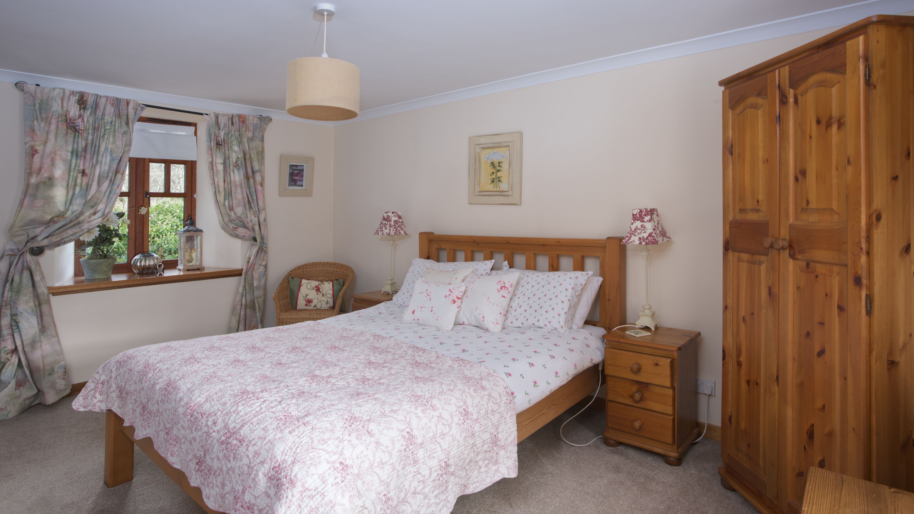 A bedroom with a wooden bed, a nightstand, a wardrobe, and a window with curtains.