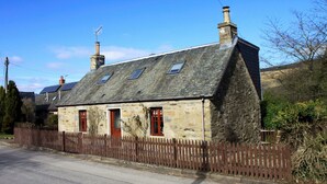 A stone house with a sloped roof, two chimneys, and a wooden fence. - Ivy Cottage, Balnaguard Detached cottage with off street parking. (Balnaguard)