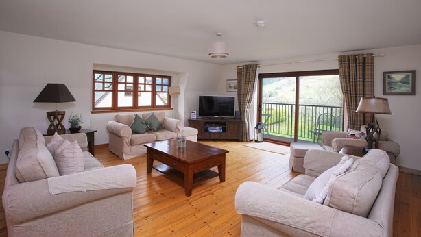 A spacious living room with a wooden floor, beige sofas, a coffee table, a TV, and a balcony with curtains. - Ivy Cottage, Balnaguard Detached cottage with off street parking. (Balnaguard)
