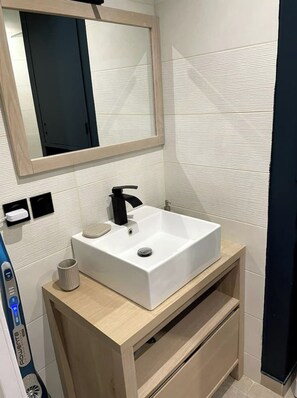 A modern bathroom with a white sink, a mirror, and a wooden vanity. - Le Méditerranée - 1st Row, Ocean View, 3* Class (1st Row, Ocean View) (Canet-en-Roussillon)