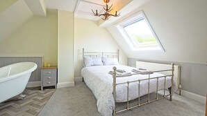 A bedroom with a sloped ceiling, a skylight, a white bed, a radiator, and a clawfoot bathtub. - Coquetdale Cottage in Rothbury, quiet village location (Rothbury)