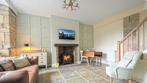 A cozy living room with a fireplace, a television mounted above it, and a stone floor. - Coquetdale Cottage in Rothbury, quiet village location (Rothbury)
