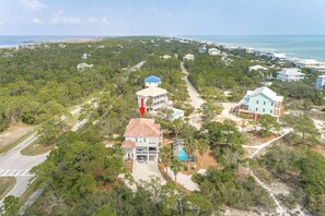 A coastal residential area with houses surrounded by dense greenery and a beach in the background.