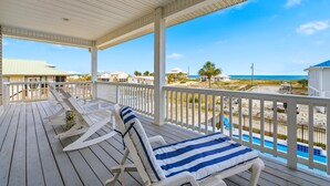 Eine überdachte Terrasse mit weißen Geländern, zwei Liegestühlen und Blick auf Strand und Meer.