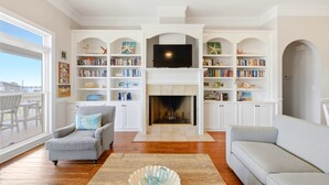 Ein Wohnzimmer mit Kamin, Bücherregalen, einem Fernseher und Ausblick nach draußen.