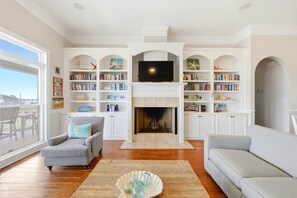 A living room with a fireplace, bookshelves, a television, and a view to the outside.
