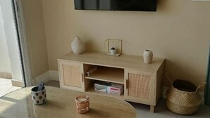 Un salon avec un téléviseur fixé au mur, un meuble en bois orné d’objets décoratifs, une table basse en verre et un panier en osier.