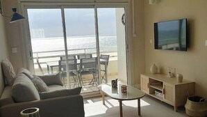 Un salon avec un canapé, une table basse et un téléviseur. Il y a un balcon avec vue sur l’océan.