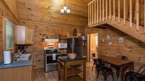 A wooden cabin interior with a kitchen, dining area, and a staircase.