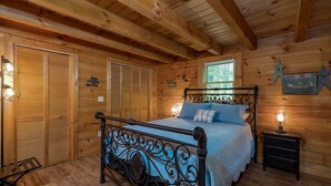 A wooden cabin bedroom with a bed, a nightstand, and a window.