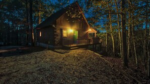 A log cabin with a porch, surrounded by trees.