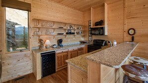 A wooden cabin kitchen with granite countertops, wooden cabinets, a built-in oven, and a window overlooking a mountainous landscape.