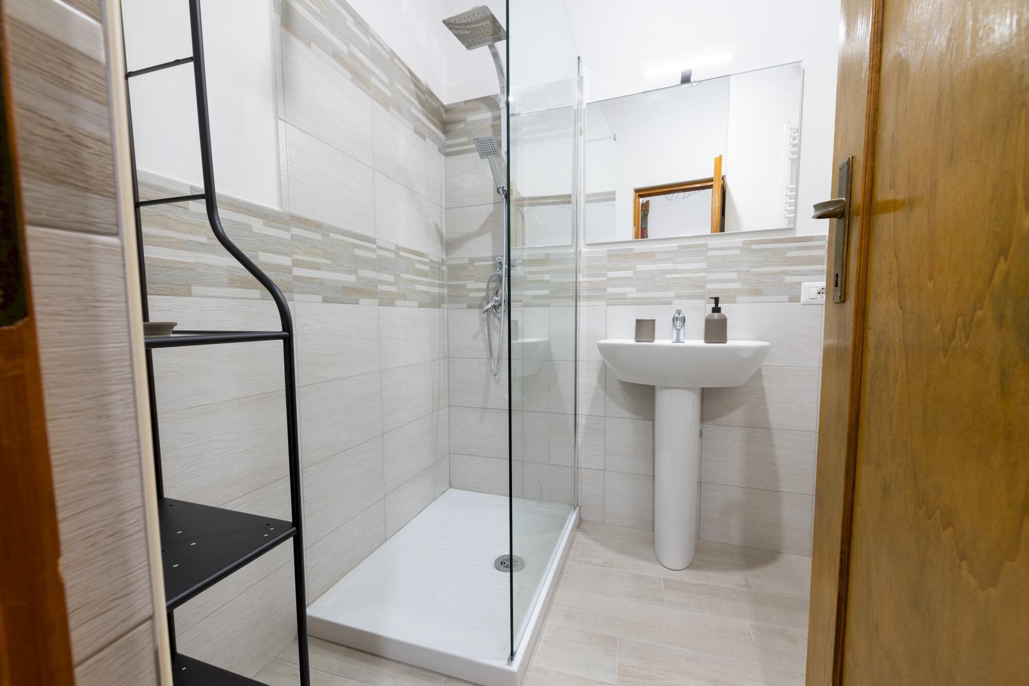 A modern bathroom with a glass shower enclosure, a white sink, and a wooden door.
