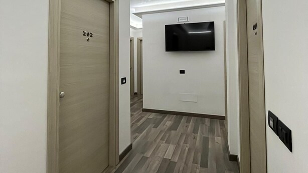 A hallway with wooden doors, a flat-screen TV mounted on the wall, and a patterned floor. - Albergo 3 Torri (Maddaloni)