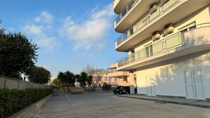 A multi-story residential building with balconies, a paved walkway, and parked cars. - Albergo 3 Torri (Maddaloni)